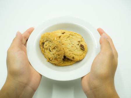 Woman's hand holding chocolate chip cookies in the white plateの写真素材