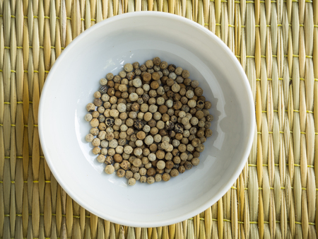 Raw pepper in the white cup on the brown matの写真素材