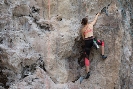 Female rock climber climbs on a rocky wallの写真素材