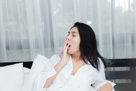 Beautiful woman waking up and yawn in her bed in the bedroom, she is stretching and smilingの写真素材