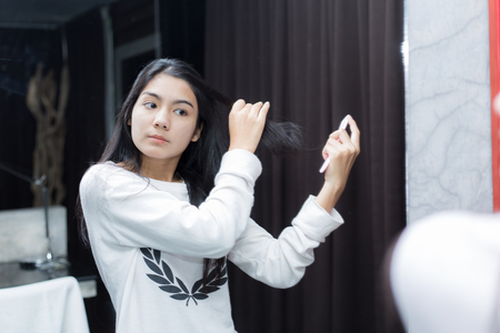 Young asian woman using curling iron before mirror at home in the morningの写真素材