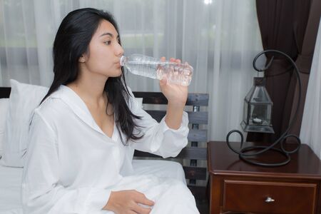 Young healthy girl drink water on her bed in the morningの写真素材