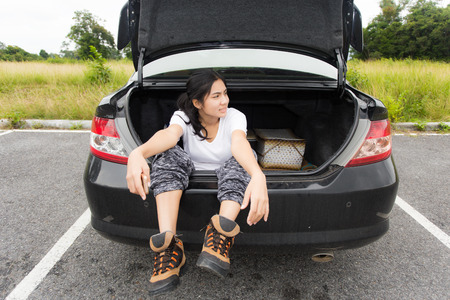 Young asian woman sitting in the car trunk on the roadの写真素材