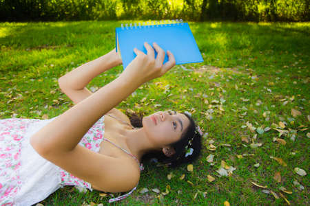 Pretty young asian woman picnic on the meadow with her book and relaxing in the park