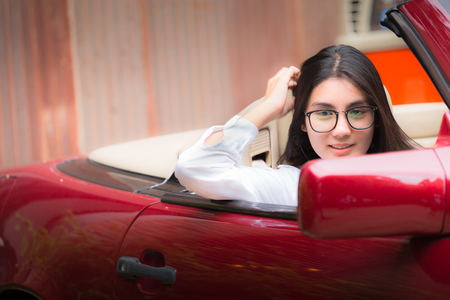 A portrait of a beautiful young asian woman wearing glasses and she is in the red carの写真素材