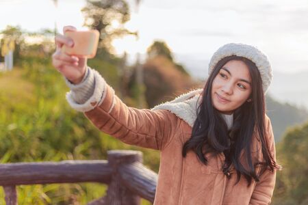 Asian woman taking photo selfie from top of the mountain in the morning with sunrise
