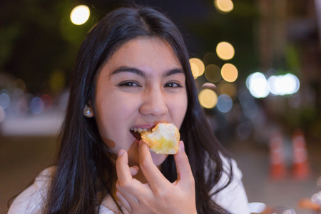 Beautiful asian woman eating sweets in the night street marketの写真素材