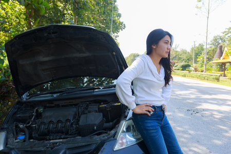 Beautiful young asian woman in the white suit with a broken car with open hood.の写真素材