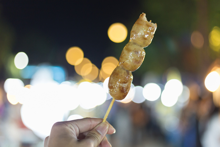 Thai style grilled pork sausage with bamboo sticks in the night market, bokeh backgroundの写真素材