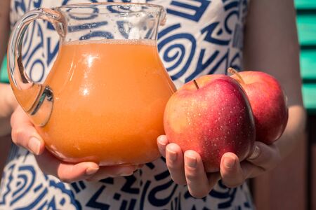 apple juice with pulp in a carafe with red apples in the hands of a young girlの写真素材
