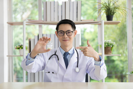 asian doctor showing capsule of vitamin or medicine in small glass bottle, for showing patient and prescription medicine before explain how to eatの写真素材