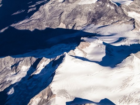 Alps, view of the snowy mountain top from the window of the plane. Land bending and nature concept.