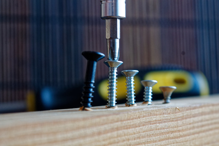 Scattered screw screwed with screwdriver into the wooden plankの写真素材