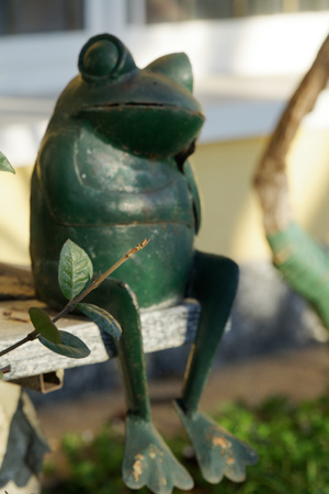 Steel green frog sits in crossed legs gesture on stone stairs. Garden statue Selective focus on the face of frogの写真素材