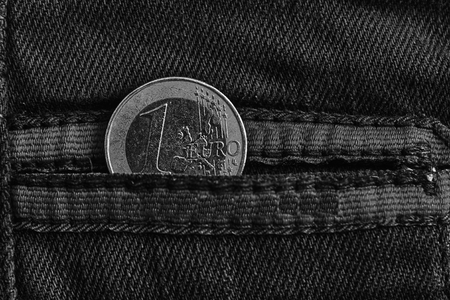 Monochrome Euro coin with a denomination of 1 euro in the pocket of worn blue denim jeans with red laces.の写真素材