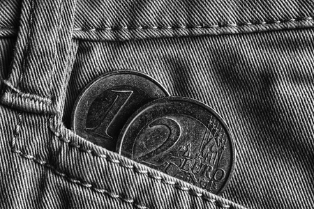 Euro coin with a denomination of one and two euro in the pocket of denim jeans, monochrome shot.の写真素材