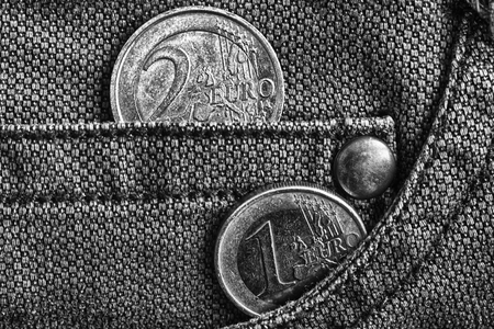 Euro coin with a denomination of 1 and 2 euro in the pocket of worn denim jeans, monochrome shot.
