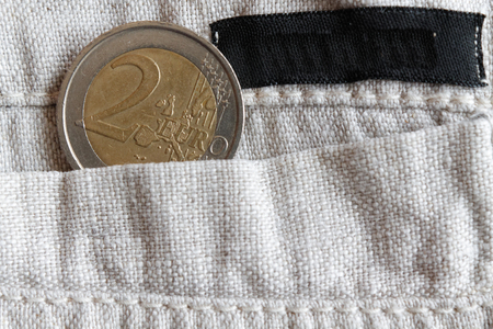 Euro coin with a denomination of 2 euro in the pocket of linen pants with black stripe