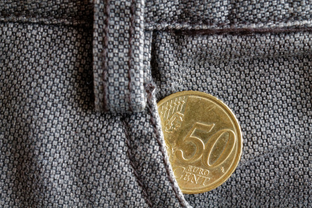 Euro coin with a denomination of fifty euro cents in the pocket of old brown denim jeans