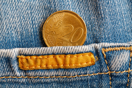 Euro coin with a denomination of twenty euro cents in the pocket of worn blue denim jeans with...