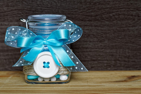 Decorative jar with bow and blue stones inside on wooden table, mockup for postcard or greeting...