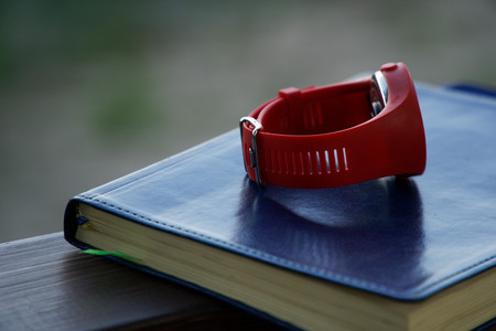 Red sport watch on Notebook lies on wooden handrail in park, business concept.の写真素材