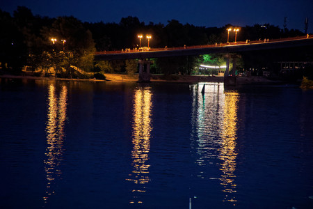 Blinking lights on night bridge, sparkle in water reflection.