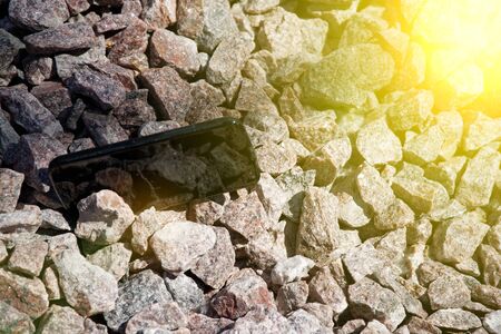 Broken cellphone abandoned and lost among the gravel and sun beam lights.の写真素材