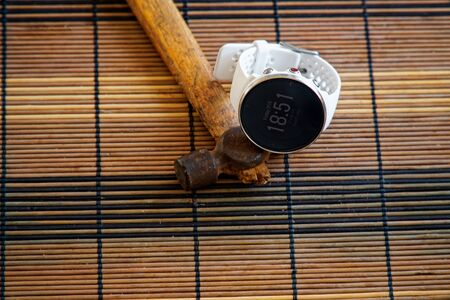 Sport watch in white color on wooden table, Smart watch for running and fitness training. Hammer with wooden handle on background.の写真素材
