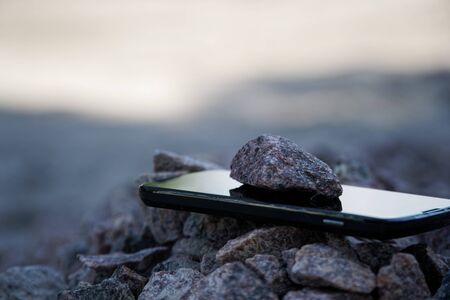 Cell phone with broken glass on gravel granite stones, unbreakable gadget.の写真素材