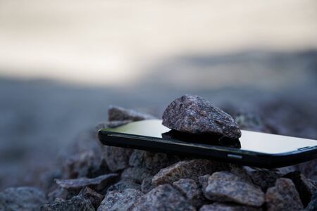 Cell phone with broken glass on gravel granite stones, unbreakable gadget.