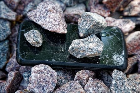 Cell phone with broken glass on gravel granite stones, unbreakable gadget.の写真素材
