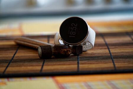 Sport watch in white color on wooden table, Smart watch for running and fitness training. Hammer with wooden handle on background.の写真素材