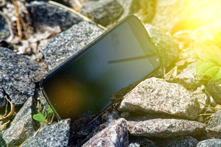 Broken cellphone abandoned and lost among the gravel, with sun beam .の写真素材