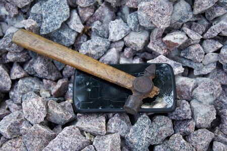Broken glass of smartphone with hammer on gravel stones. Selective focus.の写真素材
