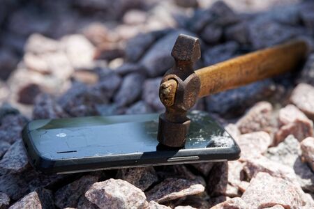 Broken glass of smartphone with hammer on gravel stones. Selective focus.の写真素材