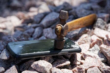 Broken glass of smartphone with hammer on gravel stones. Selective focus.の写真素材