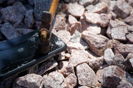Broken glass of smartphone with hammer on gravel stones. Selective focus.の写真素材