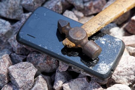 Broken glass of smartphone with hammer on gravel stones. Selective focus.の写真素材