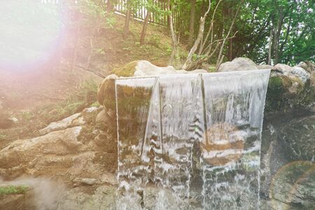 Garden waterfall of stones. Water flows through the stone. The morning sun shines on the waterfallの写真素材