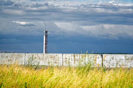 Lighthouse or old beacon under storm clouds against yellow field.の写真素材