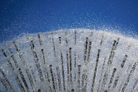 Fountain in the sun backlight against blue sky. The fountains gushing sparkling water from pipe in park.の写真素材