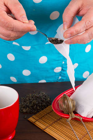 Housewife in apron putting tea in tea bags in kitchen