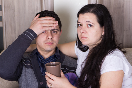 Attentive wife giving a cup of hot tea to husband with feverの写真素材