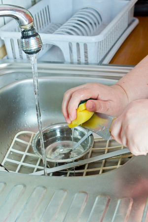 Housewife washing dishes with sponge in kitchen sinkの写真素材