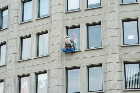 BUDAPEST, HUNGARY - JUNE 29, 2014: Industrial mountaineering worker washing windows of a modern...