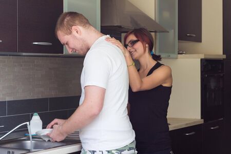 Happy guy helping girlfriend to do dishes at kitchen