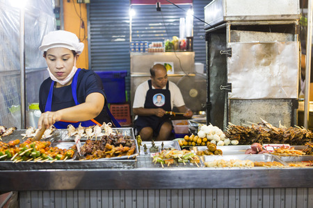 HUA HIN, THAILAND - MARCH 09, 2016: Staff preparing meat and vegetables on grill at stall with street food in local night market, Prachuap Khiri Khan Provinceのeditorial素材