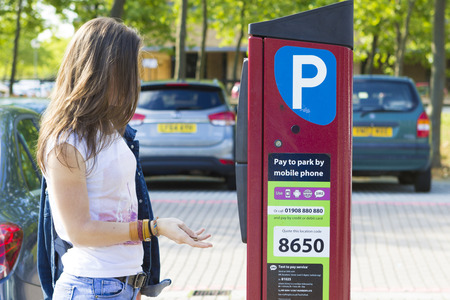MILTON KEYNES, ENGLAND - JULY 27, 2016: Female customer paying for parking the car using installed machine outdoors, UKのeditorial素材