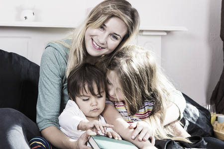 Young mother reading book to children in bedroomの写真素材